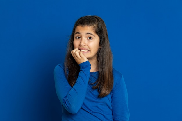 Adorable niña preadolescente con jersey azul gesticulando sobre la pared azul