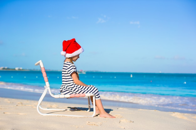 Adorable niña en rojo Santa Hat en silla de playa