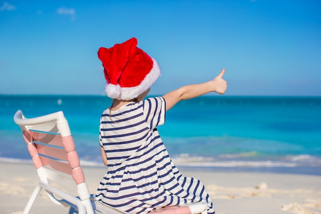 Adorable niña en rojo Santa Hat en silla de playa