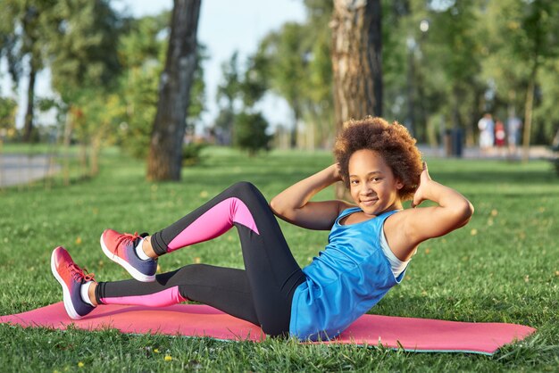 Adorable niña en ropa deportiva haciendo ejercicio en el parque