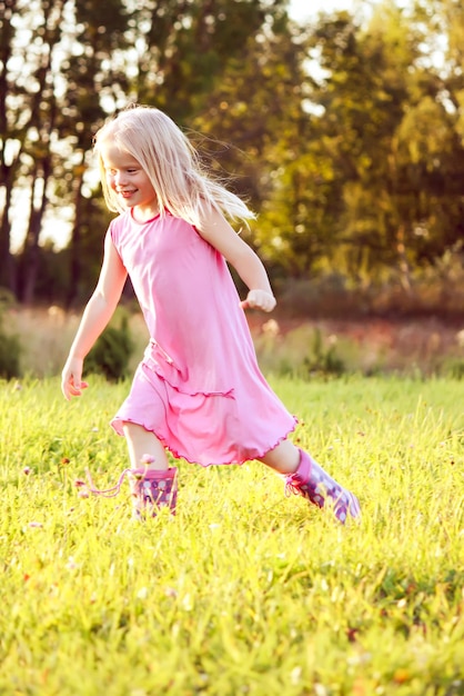 Adorable niña rubia en un prado en un día soleado de verano