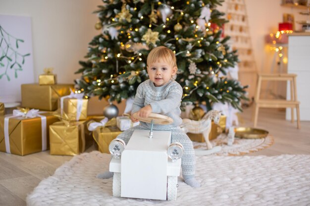 Adorable niña sentada cerca del árbol de navidad con luces festivas y regalos de navidad navidad y año nuevo