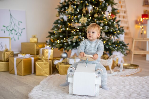 Adorable niña sentada cerca del árbol de navidad con luces festivas y regalos de navidad navidad y año nuevo