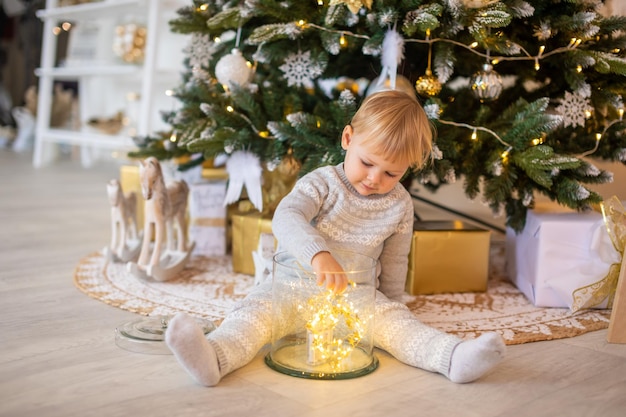 Adorable niña sentada cerca del árbol de navidad con luces festivas y regalos de navidad navidad y año nuevo