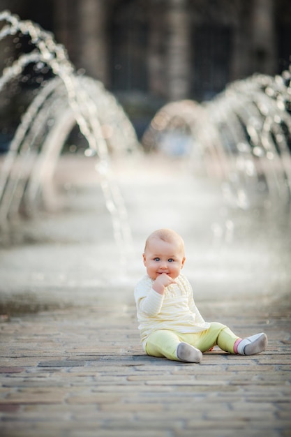 Adorable niña sentada en la plaza de la ciudad cerca de la fuente