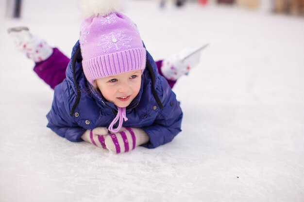 Adorable niña sentada sobre hielo con patines después de la caída