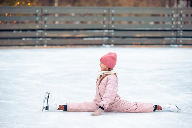 Adorable niña sentada sobre hielo con patines después del otoño