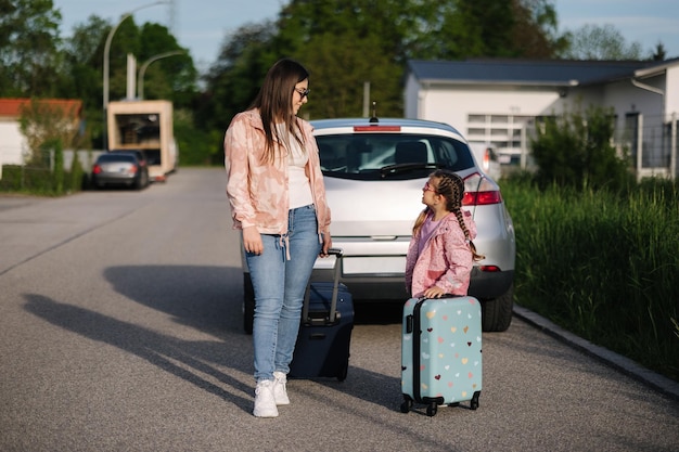 Adorable niña se sienta en su maleta de niño y espera el viaje con su madre dos hermosos