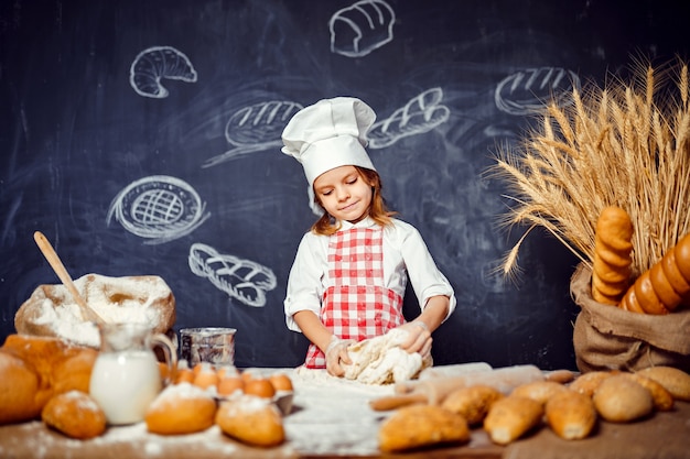 Adorable niña con sombrero de chef haciendo masa