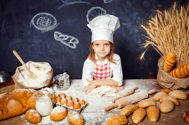 Adorable niña con sombrero de chef haciendo masa