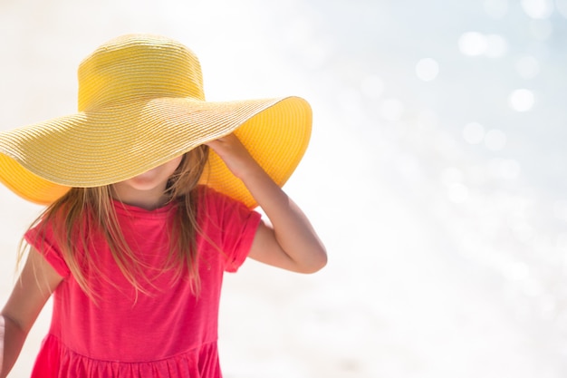 Adorable niña con sombrero en la playa durante las vacaciones de verano