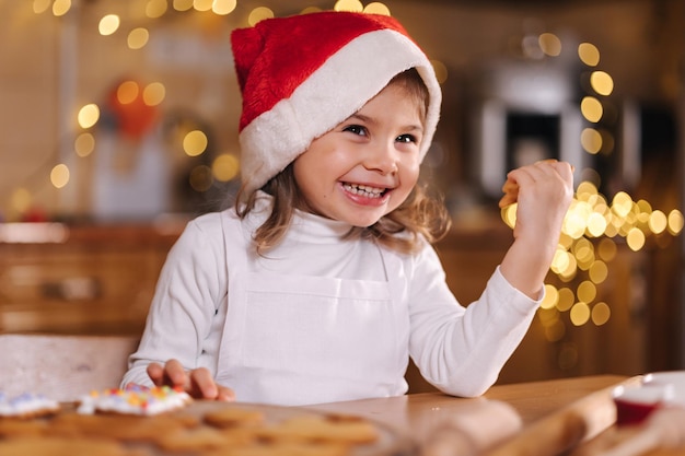 Adorable niña con sombrero de santa comiendo pan de jengibre casero y riendo niño feliz