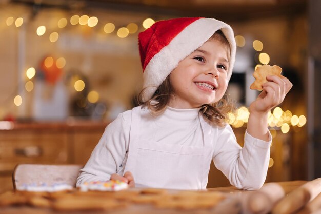 Adorable niña con sombrero de santa comiendo pan de jengibre casero y riendo niño feliz