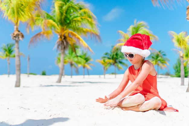 Adorable niña con sombrero de Santa durante las vacaciones de Navidad en la playa