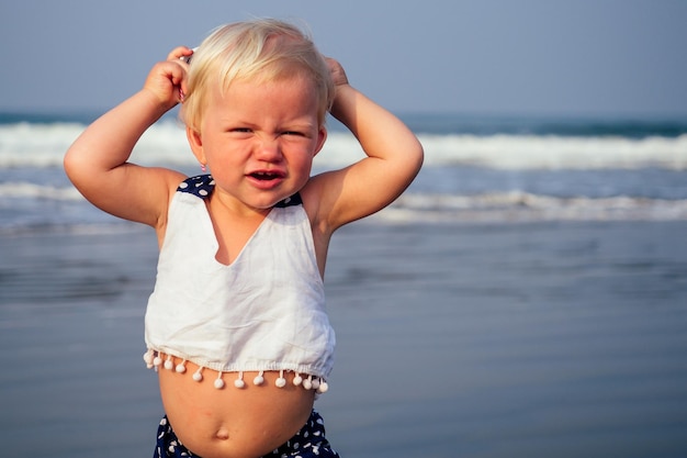 Adorable niña soñolienta en la playa aplicando crema bloqueador solar. De un año de edad bebé rubio niño dulce gran vientre hinchado vacaciones de verano alergia tropical.