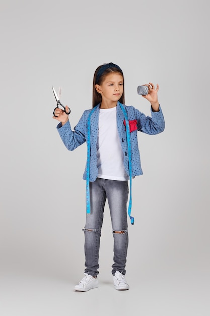 Adorable niña sosteniendo cinta métrica y carrete de hilo