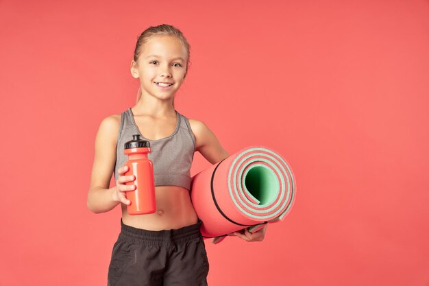 Adorable niña sosteniendo una estera de yoga y una botella de agua