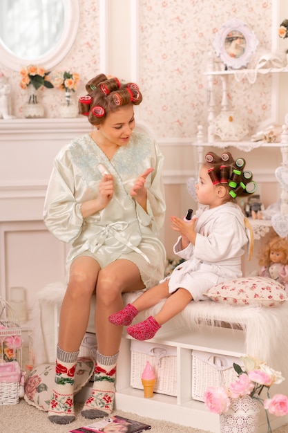 Adorable niña con su madre en rulos pintan sus uñas. Copia el comportamiento de mamá. Mamá le enseña a su hija a cuidarse sola. Bonito día.