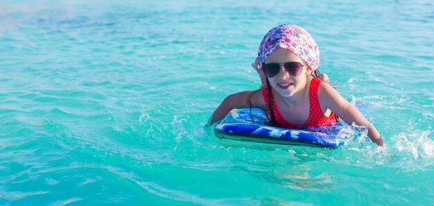 Adorable niña en una tabla de surf en el mar turquesa