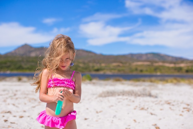 Adorable niña en traje de baño con botella de loción bronceadora