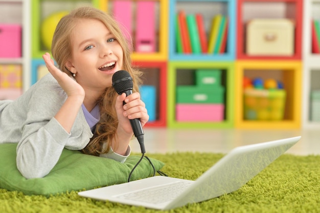 Adorable niña usando una computadora portátil moderna y cantando karaoke