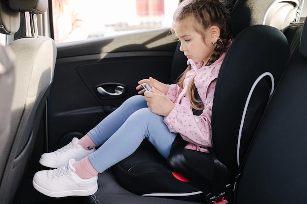 Adorable niña usando tableta en auto en asiento de auto