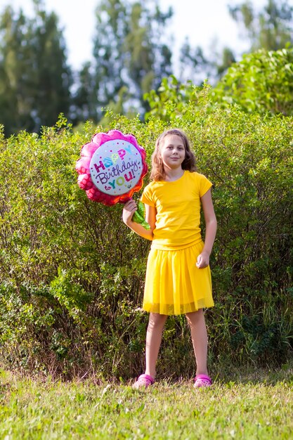 Adorable niña en vestido amarillo con globo colorido festivo feliz cumpleaños en forma de flor. Niño feliz al aire libre