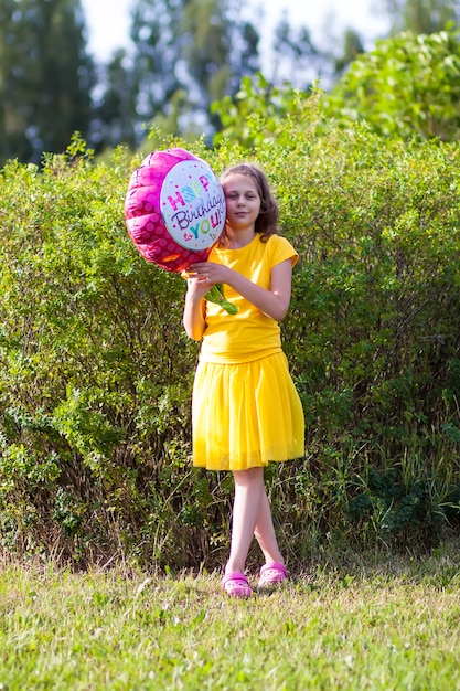 Adorable niña en vestido amarillo con globo colorido festivo feliz cumpleaños en forma de flor. Niño feliz al aire libre