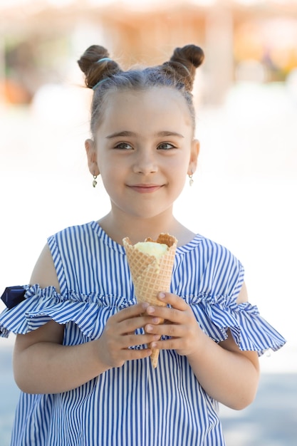 Adorable niña en vestido azul comiendo helado en el parque