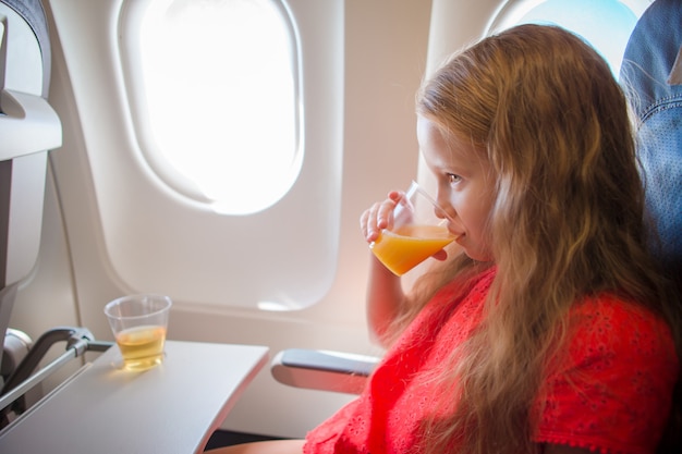 Adorable niña viaja en un avión. niño bebiendo jugo de naranja sentado cerca de la ventana del avión