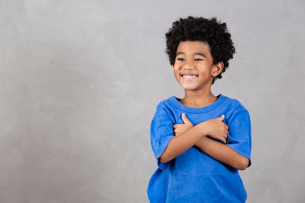 Adorable niño afro con los brazos cruzados sonriendo sobre fondo gris