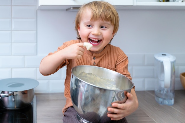 Adorable niño ayudando y horneando tarta de manzana en la cocina de casa, interior. Niño mezclando y probando masa para bizcocho. Cocinar con el concepto de niños.