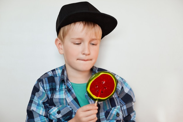 Adorable niño en camisa de moda y gorra negra mirando gran paleta de colores. Lindo colegial vistiendo de moda