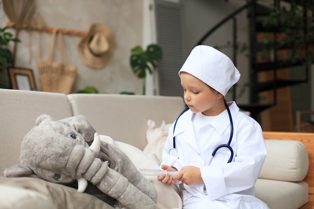 Adorable niño disfrazado de médico jugando con elefante de juguete, controlando su respiración con estetoscopio.