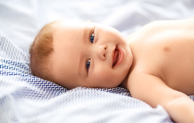 Adorable niño en dormitorio soleado. Niño recién nacido relajante en la cama.