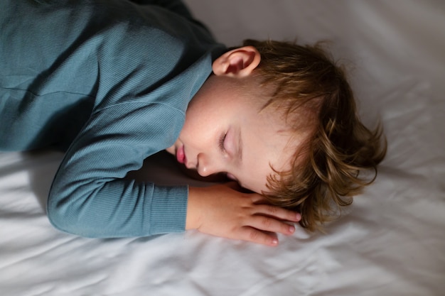 Adorable niño está durmiendo en su cama en la oscuridad en casa. Hora de acostarse. Niño descansando y soñando por la noche.