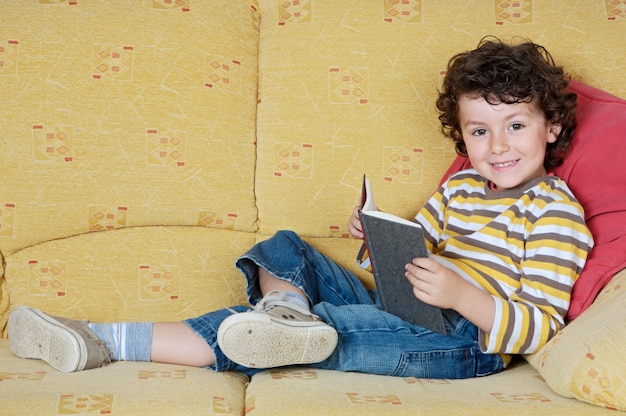 Adorable niño feliz leyendo en el sillón de tu casa.