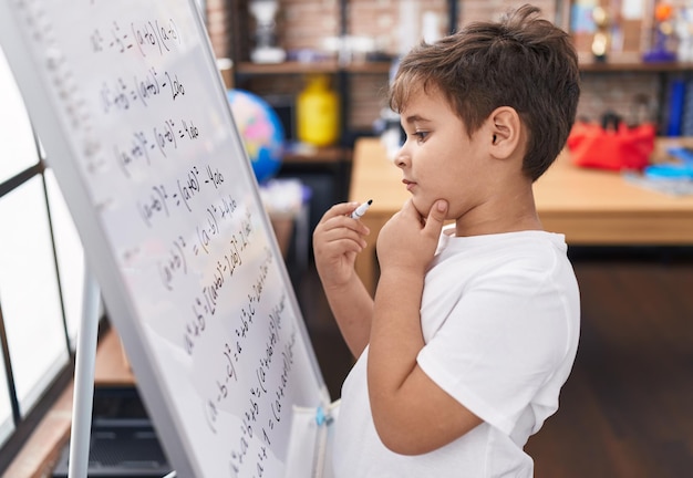 Adorable niño hispano estudiante de preescolar escribiendo en la pizarra en el aula
