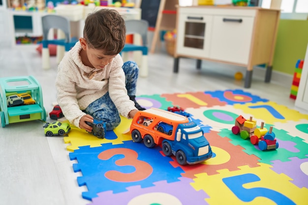 Adorable niño hispano jugando con coches de juguete sentado en el suelo en el jardín de infantes