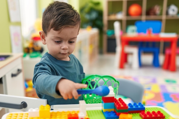 Adorable niño hispano jugando con cocina de juego de pie en el jardín de infantes