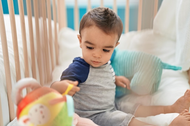 Adorable niño hispano sentado en la cuna con expresión relajada en el dormitorio