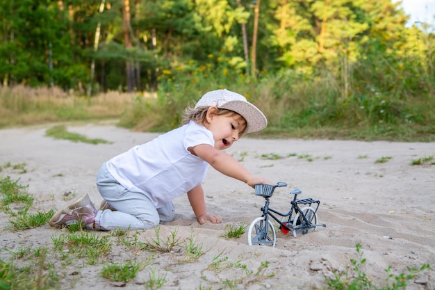 Adorable niño juega con una bicicleta de juguete en la naturaleza niño a cuatro patas en la arena del césped