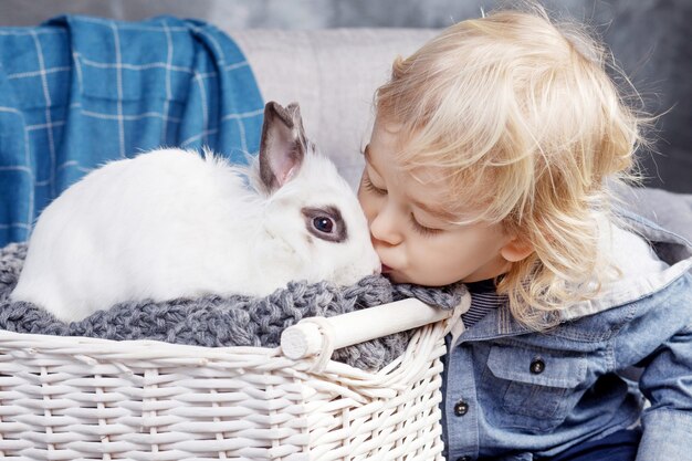 Adorable niño juega con un conejo blanco. El chico besa a un conejo