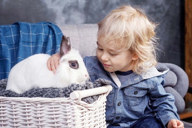 Adorable niño juega con un conejo blanco. El niño mira un conejo