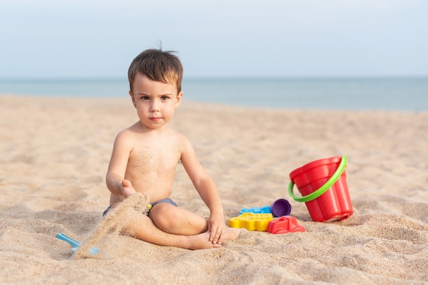 Adorable niño juega en la orilla del mar en la arena con juguetes Vacaciones de verano