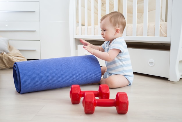 Adorable niño jugando con pesas y colchoneta de fitness