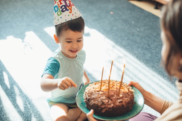 Adorable niño lleva gorro de fiesta mientras la madre le da un pastel de cumpleaños