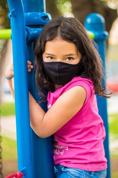 Adorable niño con mascarilla y jugando en el patio de recreo