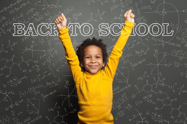 Adorable niño negro estudiante inteligente niño en el fondo de la pizarra concepto de regreso a la escuela