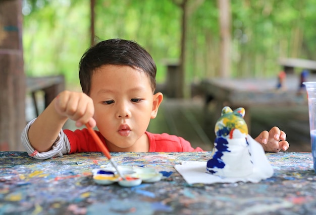 Adorable niño pequeño asiático pintando en una muñeca de estuco